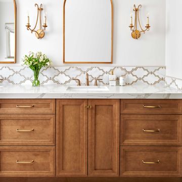 bathroom, white walls, brown cabinets, white marble countertops, gold sconces and gold mirror