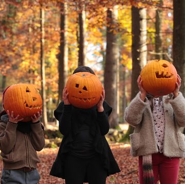 two girls and a boy are playing halloween in the woods, covering their faces with carved pumpkins