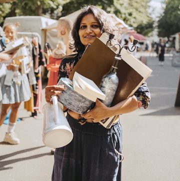 portrait of smiling woman holding various merchandise while standing at flea market