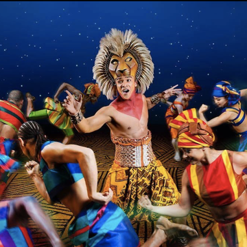actor dressed as lion surrounded by dancers in 'the lion king' on broadway